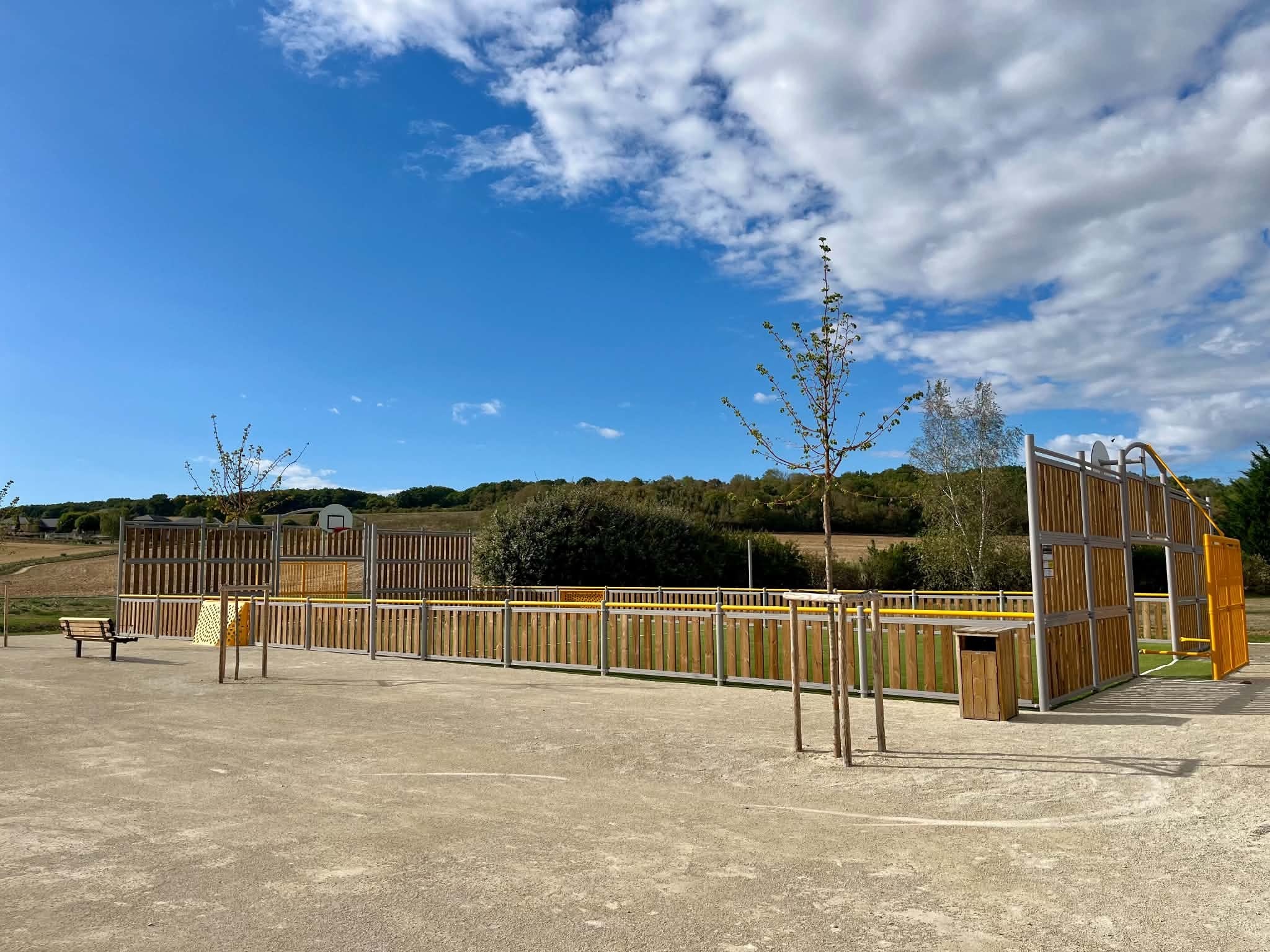 L’aire de jeux du parc de Muzy : structures en bois, bancs et clôture, sous un ciel d’été