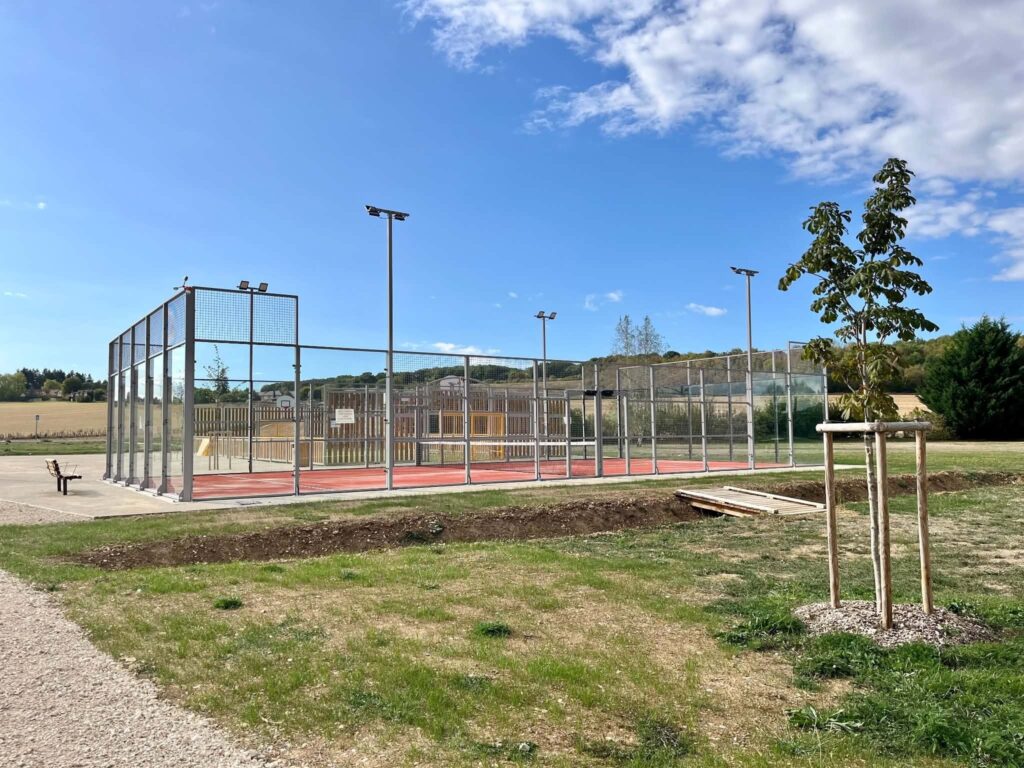 Le terrain de padel du parc de Muzy, clôturé de parois vitrées, et la prairie plantée alentour